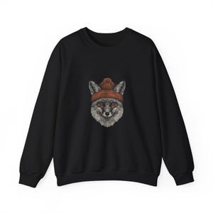 May include: Black sweatshirt featuring a detailed illustration of a fox wearing a rust-colored beanie. The fox has gray and white fur with orange eyes. The sweatshirt has long sleeves and a crew neck.