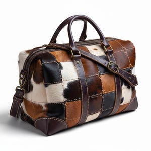 May include: A patchwork leather duffel bag with a mix of brown, black, and white cowhide squares. It features dark brown leather handles, a shoulder strap, and a zipper closure. The bag has a rectangular shape and is designed for travel.