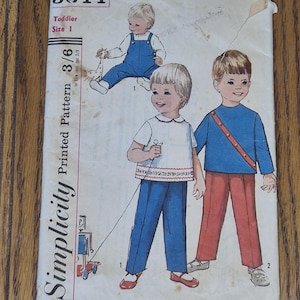Puede incluir: Un sobre de patrón de costura vintage Simplicity 5644 para niños pequeños talla 1. El frente presenta ilustraciones de niños con overoles, una blusa blanca con pantalones azules y una blusa azul con pantalones rojos, junto al texto Simplicity 5644.