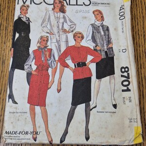 May include: A vintage McCall's 8701 sewing pattern envelope featuring illustrations of five different outfits including dresses, skirts, and jackets. The white paper envelope displays the text McCall's, SP335, and size 12, bust 34, with visible age-related staining.
