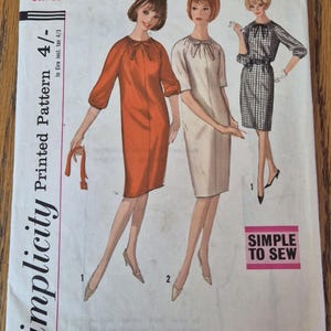 Può includere: Una busta per cartamodello Simplicity 5578 per taglia adolescente 12t, busto 32. Il fronte presenta illustrazioni di tre abiti: uno arancione, uno bianco e uno a scacchi bianchi e neri, tutti con dettagli a fiocco sullo scollo.