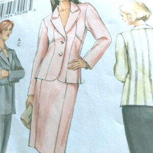 Può includere: Illustrazione di moda di un tailleur gonna rosa chiaro con un blazer a due bottoni e una gonna al ginocchio. Il disegno mostra una donna con i capelli scuri e una pochette. Il modello è etichettato V8045.