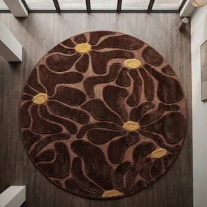 Può includere: Un tappeto circolare con uno sfondo marrone scuro e un motivo floreale in rilievo e testurizzato. Il design è composto da grandi petali astratti marrone scuro che si irradiano da piccoli centri testurizzati color giallo senape.