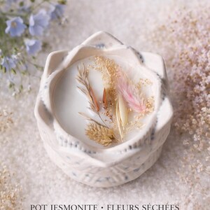 May include: A white ceramic candle in a decorative holder, with dried flowers and a pink feather. The candle is scented with flax flower fragrance. The text "Nancy Candle House" is at the top.