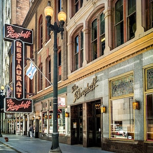 Könnte beinhalten: Die Außenfassade des Restaurants The Berghoff zeigt ein markantes vertikales Neonschild mit roter Schrift, große Bogenfenster, steinerne Fassadendetails und einen schwarzen Metall-Laternenpfahl auf einem Bürgersteig in Chicago.