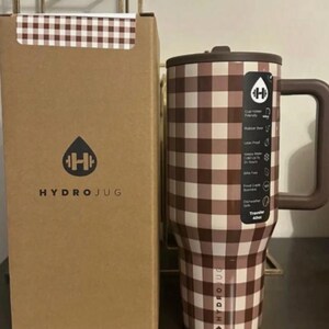 May include: A brown and white checkered Hydrojug tumbler with a handle and a matching box. The tumbler has a brown lid and handle. The box has the Hydrojug logo and text. The tumbler is designed to hold 40oz.