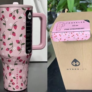 May include: Pink HydroJug water bottle with a handle, featuring a strawberry and floral pattern. The bottle has a lid and a large handle. The packaging label reads "Traveler 32 oz Pink Strawberry". The HydroJug logo is visible.