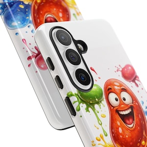 May include: White phone case with a colorful cartoon design featuring a smiling, orange bean-shaped character with a wide grin. The design includes splashes of green, yellow, red, and blue paint.