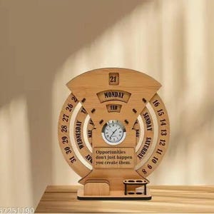 Può includere: Calendario perpetuo in legno con orologio e portapenne. Il calendario mostra il giorno, la data e il mese. Il testo "Opportunities don't just happen you create them" è visibile. Il calendario è in legno marrone chiaro.