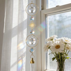 May include: A decorative suncatcher with a gold chain, hoops, and accents. The suncatcher features clear crystal spheres, faceted crystals, and a gold sunburst charm. A clear glass tube hangs at the bottom.