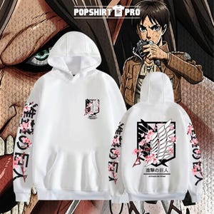 Può includere: Felpa con cappuccio bianca con un design grafico anteriore e posteriore. La parte anteriore presenta un emblema in bianco e nero con accenti floreali rosa. Le maniche hanno testo giapponese e fiori rosa. Il retro ha la scritta "ATTACK ON TITAN".