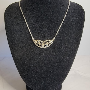 May include: A gold-tone necklace featuring a crescent-shaped pendant with a decorative filigree border. The pendant is inlaid with multiple black marquise-cut stones and small clear round stones arranged in a symmetrical floral-inspired pattern.