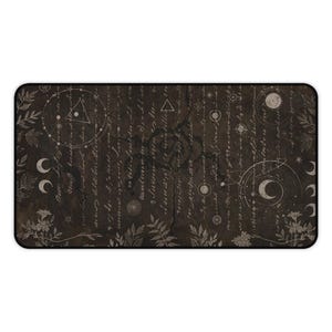 May include: A rectangular desk mat with a dark brown background featuring a celestial design. The design includes moons, stars, geometric shapes, and handwritten script. The mat is bordered with a black edge and floral accents.