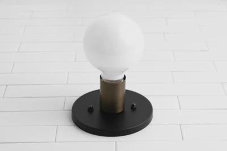 May include: A modern wall sconce featuring a large, round, white light bulb. The bulb is set in a brass-colored cylinder, which is mounted on a black, circular base. The fixture is designed for indoor use.