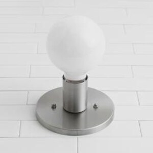 May include: A modern, round, brushed nickel wall sconce with a large, white, globe-shaped light bulb. The sconce has a circular base and a cylindrical stem. The light fixture is mounted on a white tiled wall.