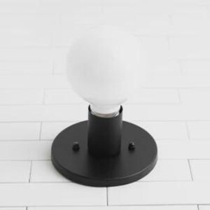 May include: A black, round wall sconce with a white, globe-shaped light bulb. The sconce has a cylindrical base and is mounted on a circular plate. The light fixture is designed for indoor use.