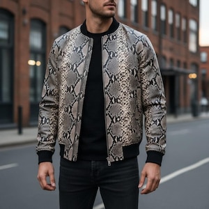 Peut inclure: Un blouson bomber avec un motif peau de serpent dans des tons beige, gris et noir. Le blouson présente un col côtelé noir, des poignets côtelés noirs et une fermeture éclair centrale argentée, porté sur un t-shirt noir et un jean gris foncé.