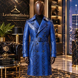 May include: A double-breasted trench coat in a vibrant blue colour featuring a black snakeskin pattern. The coat includes a matching belt with a buckle, wide lapels, shoulder epaulets, and buttoned cuffs, displayed on a headless mannequin.