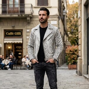Può includere: Una giacca da motociclista in pelle con motivo a pelle di serpente grigio chiaro e bianco, dotata di revers dentellato, cerniere in metallo color argento e chiusura frontale diagonale. Indossata sopra una t-shirt nera a girocollo e jeans grigio scuro consumati.