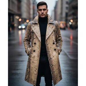 Op de afbeelding: Een dubbelrijïge trenchcoat met een beige en bruin slangenleerpatroon, brede revers en donkere knopen. De jas wordt gedragen over een zwarte coltrui en een zwarte broek, wat zorgt voor een gestructureerd silhouet met lange mouwen.
