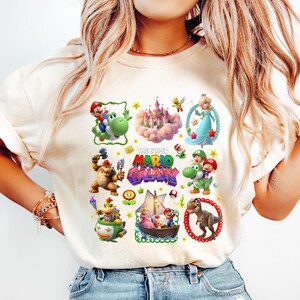 以下が含まれることがあります： スーパーマリオギャラクシーのキャラクターが描かれた、クリーム色のTシャツ。マリオ、ヨッシー、ピーチ姫、恐竜などがデザインされています。「THE SUPER MARIO GALAXY」の文字も確認できます。