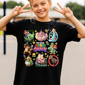 以下が含まれることがあります： 黒いTシャツ。カラフルなグラフィックデザインで、キャラクターと「THE SUPER MARIO GALAXY」の文字が描かれています。デザインには、マリオ、ヨッシー、ピーチ姫、その他のスーパーマリオのビデオゲームシリーズのキャラクターが含まれています。