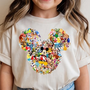 Puede incluir: Una camiseta color crema con un gran dise&ntilde;o de cabeza de Mickey Mouse lleno de varios personajes de Disney. El dise&ntilde;o incluye personajes de pel&iacute;culas cl&aacute;sicas y modernas de Disney, creando un gr&aacute;fico colorido y detallado.