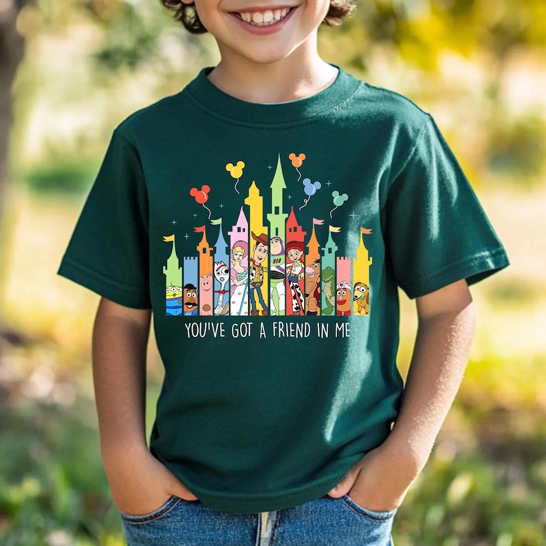 May include: Dark green t-shirt featuring a colorful graphic of cartoon characters and castles. The text "YOU'VE GOT A FRIEND IN ME" is printed at the bottom. The design includes balloons in the sky.