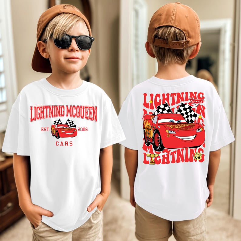 May include: White t-shirt featuring Lightning McQueen from the Cars movie. The front design includes the text "Lightning McQueen" and a graphic of the car. The back of the shirt has a larger graphic of McQueen with checkered flags.