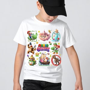 以下が含まれることがあります： スーパーマリオギャラクシーのビデオゲームのキャラクターのカラフルなグラフィックが特徴の白いTシャツ。デザインには、マリオ、ヨッシー、ピーチ姫、その他の象徴的な要素が含まれています。「MARIO GALAXY」の文字も表示されています。