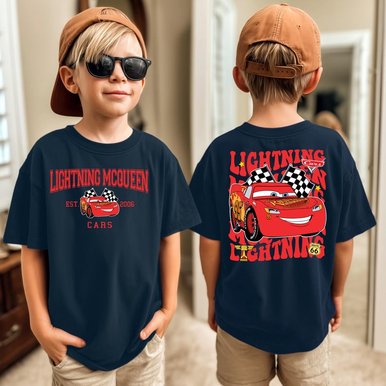 May include: Navy blue t-shirt featuring Lightning McQueen from the Cars movie. The front of the shirt displays the text "Lightning McQueen Cars Est. 2006" with an image of the red race car. The back of the shirt has a larger image of Lightning McQueen.