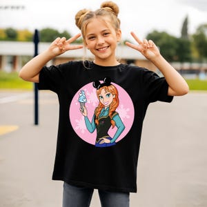 May include: Black t-shirt featuring a cartoon illustration of a character holding an ice cream cone, set against a pink circle with snowflake accents. The character has red hair and is wearing a black top and blue sleeves.
