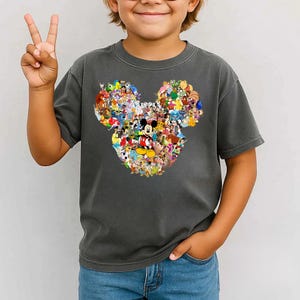 Puede incluir: Camiseta gris oscuro con un dise&ntilde;o de la cabeza de Mickey Mouse compuesto por coloridos personajes de Disney. La camiseta la lleva un ni&ntilde;o que hace el signo de la paz. Es una prenda informal de manga corta.