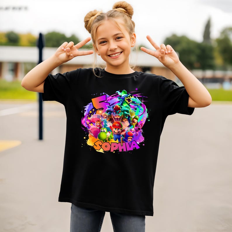 Puede incluir: Una camiseta negra de manga corta con un estampado gr&aacute;fico colorido de varios personajes de videojuegos, incluyendo a Mario, Yoshi y Bowser. El dise&ntilde;o incluye un n&uacute;mero 5 grande y el nombre SOPHIA en letras llamativas y multicolores.