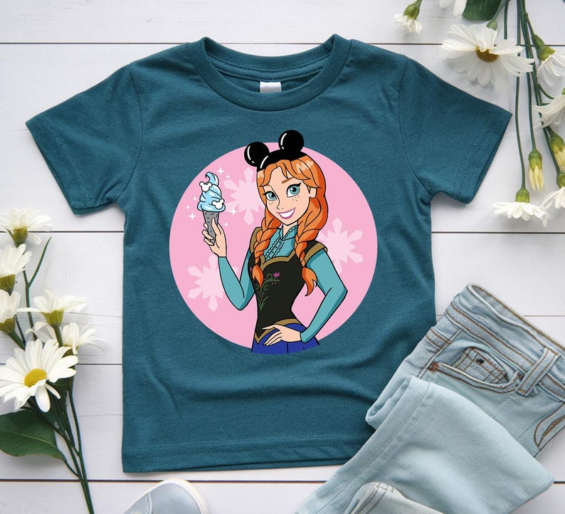 May include: Teal t-shirt featuring a cartoon illustration of a character with red hair, wearing a black top and blue skirt, holding a blue ice cream cone. The character is set against a pink circle with snowflake accents, and wears black mouse ears.
