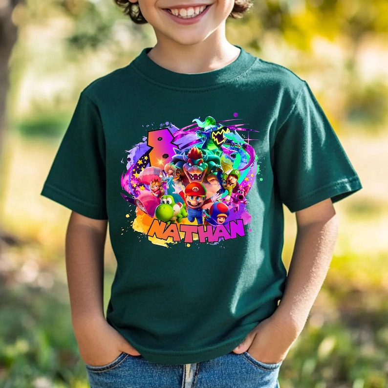 Puede incluir: Una camiseta de manga corta de color verde oscuro con un estampado gr&aacute;fico colorido de varios personajes de videojuegos, incluidos Mario, Luigi, Yoshi y Bowser. El dise&ntilde;o incluye un n&uacute;mero 8 grande y el nombre NATHAN en letras moradas.