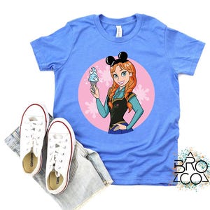 May include: A light blue t-shirt featuring a cartoon image of Anna from Frozen, holding an ice cream cone. The design is set within a pink circle with floral accents. White sneakers and denim shorts are placed below the shirt.