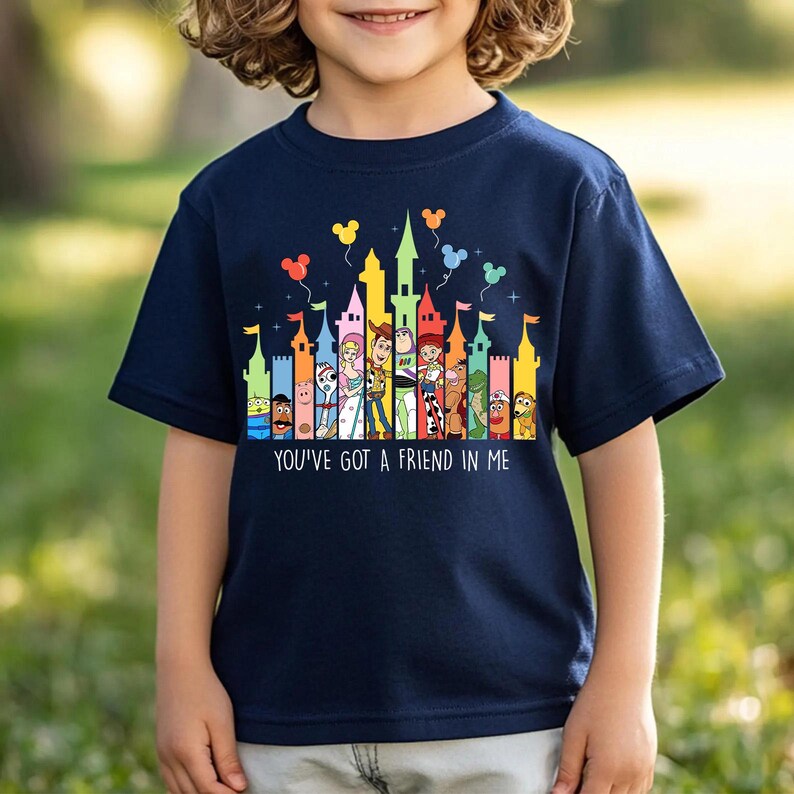 May include: Navy blue t-shirt featuring a colorful graphic of a castle skyline with cartoon characters and balloons. The text "YOU'VE GOT A FRIEND IN ME" is printed below the graphic. The shirt is worn by a child.