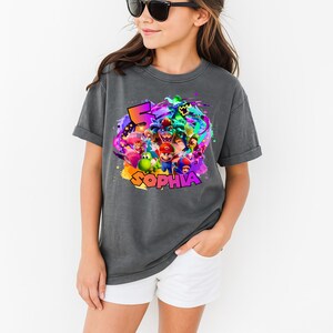Puede incluir: Una camiseta gris carb&oacute;n de manga corta con un estampado gr&aacute;fico colorido de varios personajes de videojuegos, incluidos Mario, Luigi, Yoshi y Bowser. El dise&ntilde;o incluye un n&uacute;mero 5 grande y el nombre SOPHIA en letras gruesas y cuadradas.