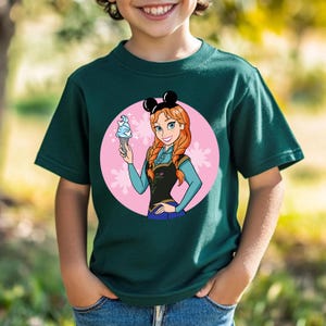 May include: Dark green t-shirt featuring a cartoon image of a character holding an ice cream cone. The character has red hair and is wearing a black and blue outfit. The image is set against a pink circle with white floral accents. The shirt also has black mouse ears.