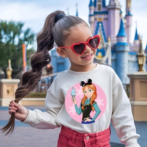 May include: A young person wearing a white sweatshirt featuring a cartoon image of Anna from Frozen holding an ice cream cone. The sweatshirt has a pink circle background with snowflakes. The person is also wearing red heart-shaped sunglasses and pink pants.