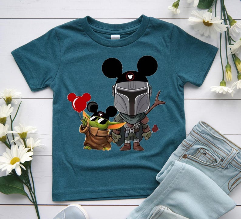 May include: Teal blue t-shirt featuring a cartoon illustration of The Mandalorian and Grogu, both wearing Mickey Mouse ears. Grogu holds a red balloon. The Mandalorian holds a twig and a red rose.