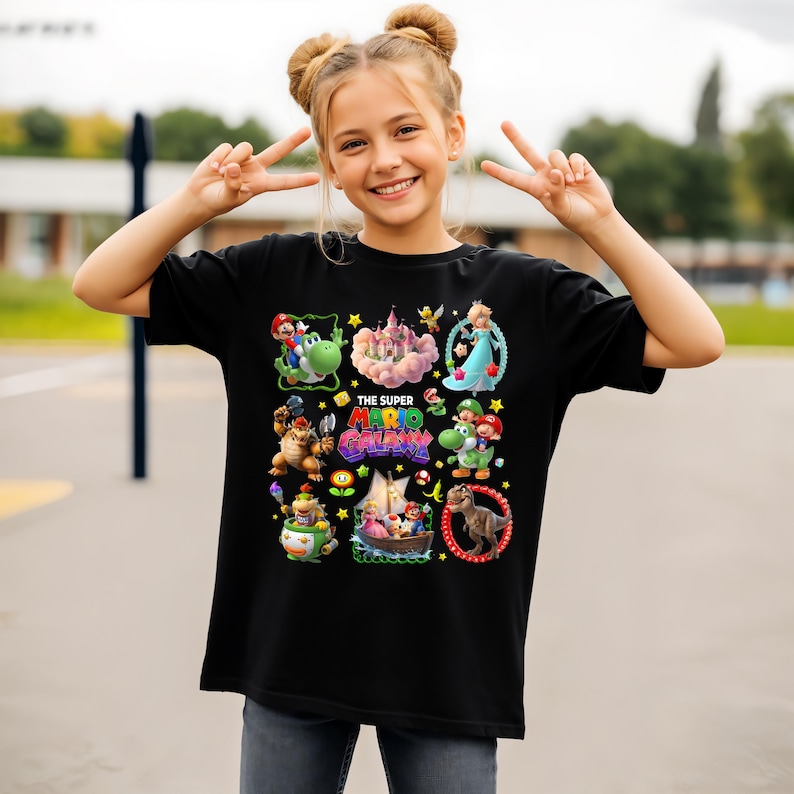 以下が含まれることがあります： 黒いTシャツ。カラフルなグラフィックデザインで、キャラクターと「THE SUPER MARIO GALAXY」の文字が描かれています。デザインには、マリオ、ヨッシー、ピーチ姫、その他のスーパーマリオのビデオゲームシリーズのキャラクターが含まれています。
