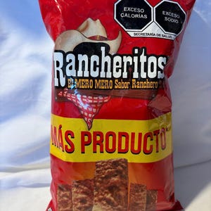 Puede incluir: Una bolsa roja de snacks Rancheritos. La bolsa presenta un gráfico de sombrero de vaquero y el texto "Rancheritos" en letras grandes. La bolsa también tiene el texto "MÁS PRODUCTO" en letras amarillas.