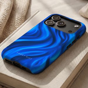 Könnte beinhalten: Eine Smartphone-Hülle mit einem leuchtend blauen, abstrakten Wellenmuster und glänzender Oberfläche. Die Hülle hat einen schwarzen Kameraausschnitt mit drei kreisförmigen Linsen und einem Blitz. Der Text SWEET RIOT ist in kleinen weißen Buchstaben aufgedruckt.