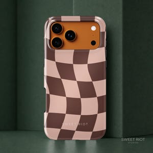 Peut inclure: Une coque de smartphone arborant un motif en damier ondulé et déformé dans des tons marron foncé et beige clair. La zone de découpe de l'appareil photo est orange uni. Le texte SWEET RIOT est imprimé en petites lettres blanches en bas.