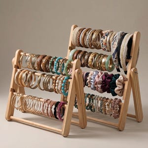 Pode incluir: Dois organizadores de joias em madeira estilo ábaco exibindo uma variedade de pulseiras, braceletes e scrunchies. As pulseiras são feitas de madeira, metal e contas. Scrunchies em várias cores também são exibidos.