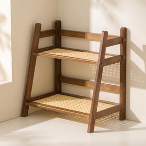 Könnte beinhalten: Ein zweistöckiges Holzregal mit dunkelbraunem Finish. Die Regale bestehen aus gewebtem, naturfarbenem Material. Das Regal ist für eine Ecke konzipiert, mit einem leiterartigen Rahmen an den Seiten.