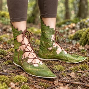 Puede incluir: Un par de botas hasta el tobillo de color verde vibrante, diseñadas con un patrón de hojas superpuestas. Las botas tienen una punta afilada y se aseguran con cordones finos de color marrón que se cruzan por la parte delantera.