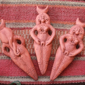 Op de afbeelding: Drie terracotta beeldjes van vrouwen met halve maan hoofdtooien. Elk beeldje heeft een andere pose en heeft ingewikkelde details, waaronder een spiraalvormig ontwerp op de buik.